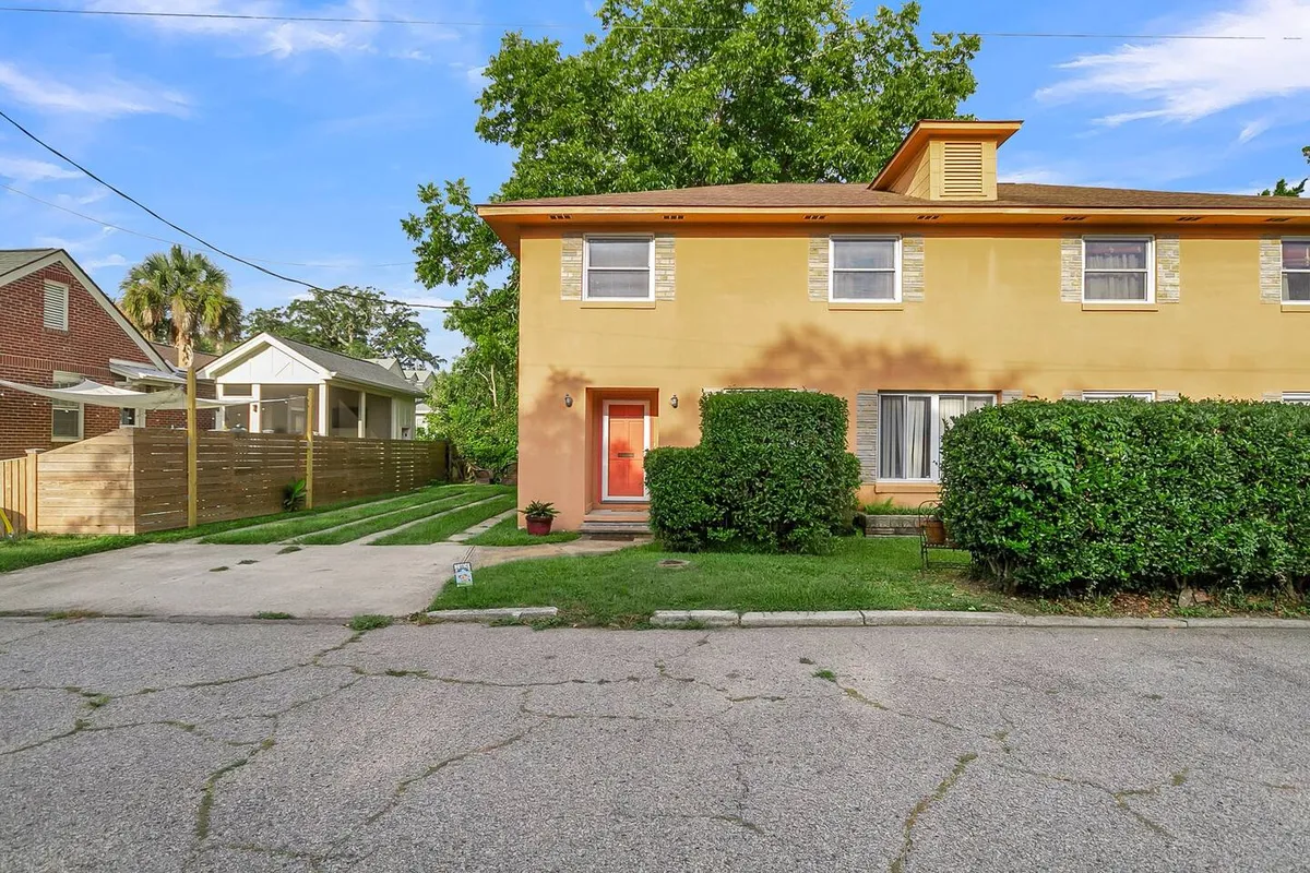 This image shows the brightly painted yellow exterior of the home, featuring a red front door and green shrubs framing the entrance. The spacious lawn is ideal for children to play and for family activities, while the welcoming porch offers a place to relax and watch the sunset.