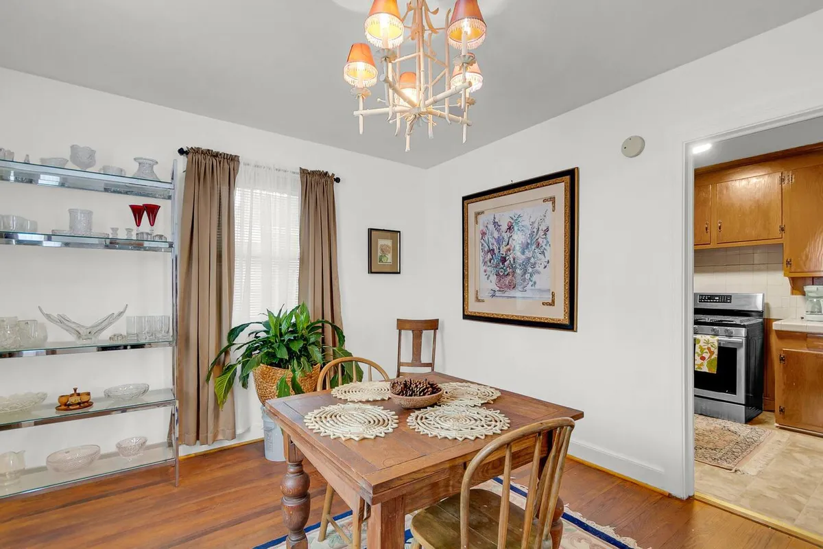 A warm, cozy dining space inside the townhouse, centered around a wood dining table and chandelier, with a shelf of glassware and inviting décor. The space evokes togetherness and communal enjoyment.