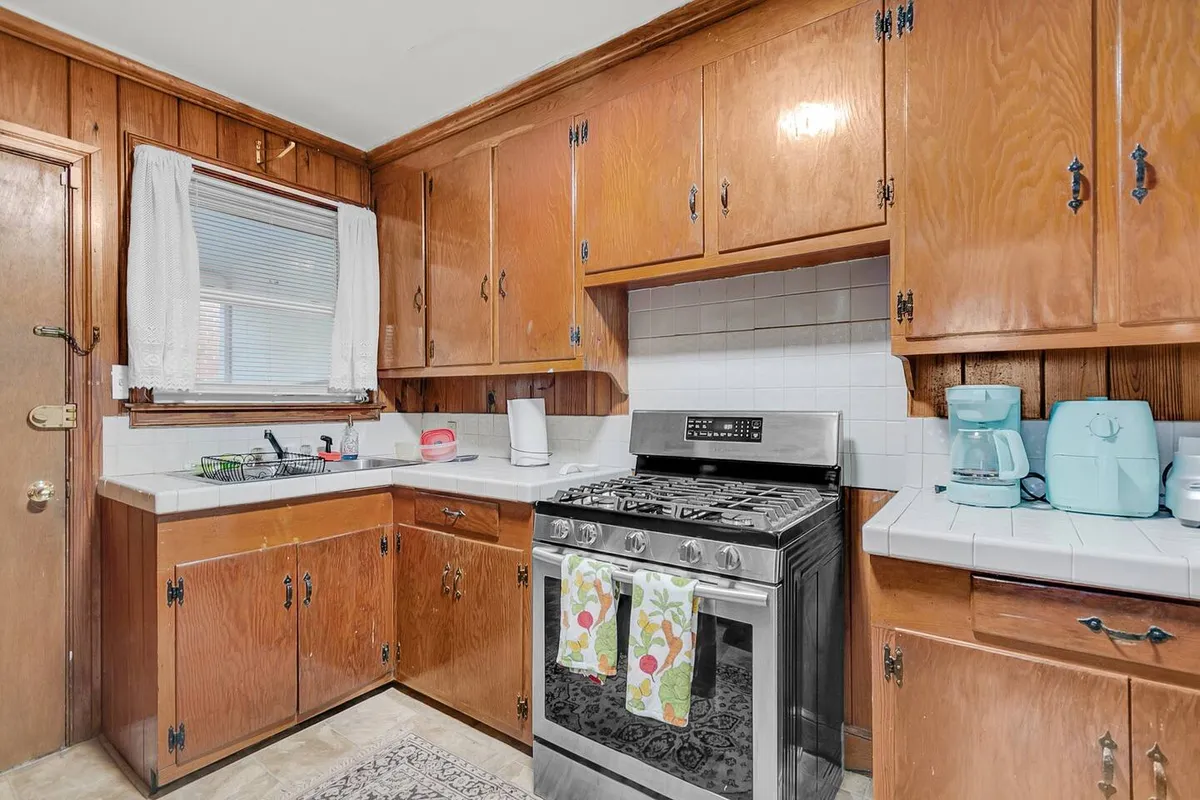A cozy kitchen scene with a stainless steel stove, wooden cabinetry, vibrant dish towels, and a selection of kitchen appliances on the counters. The countertop is spacious, highlighting the potential for meal prep and social cooking.