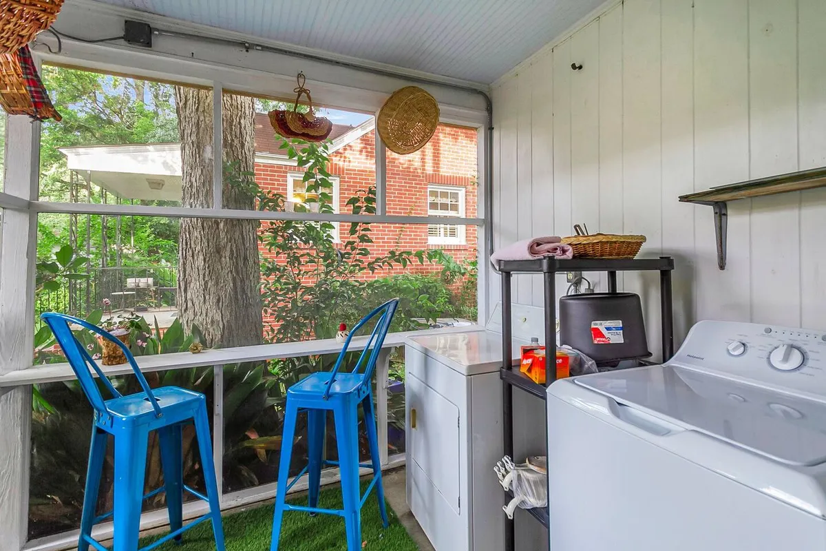 A cheerful laundry nook featuring blue chairs, a full-size washing machine, and a window offering a view outside. The setup has a relaxing mood, showing the practicality of having laundry facilities within the home.