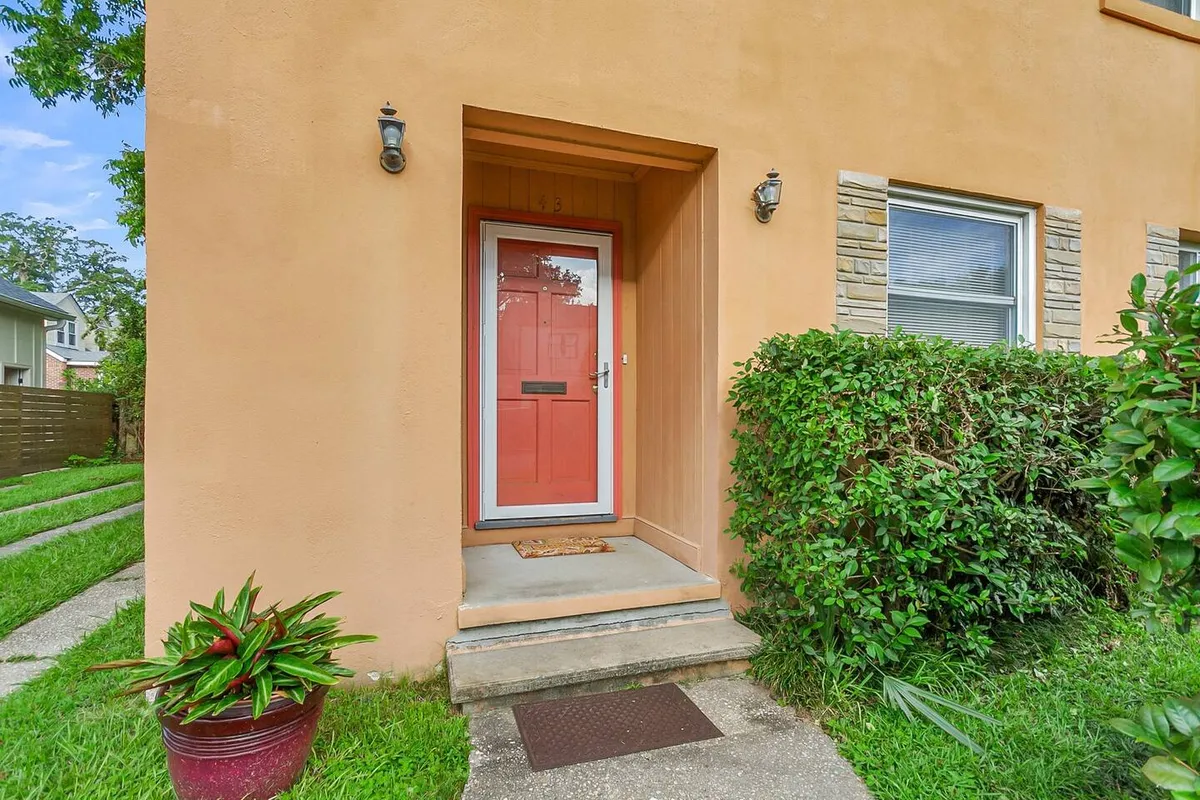A close-up exterior view of the red front door framed by greenery and stone accents, offering a sense of arrival and an inviting entrance for guests. The setting suggests festive occasions and warm greetings.