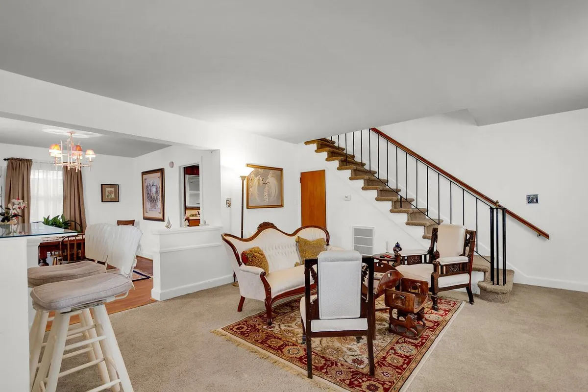 A cozy living area with a stylish staircase, soft sofa, framed artwork, and a textured rug. The room exudes warmth and is arranged for gatherings, relaxation, and milestone celebrations, emphasizing a sense of togetherness.