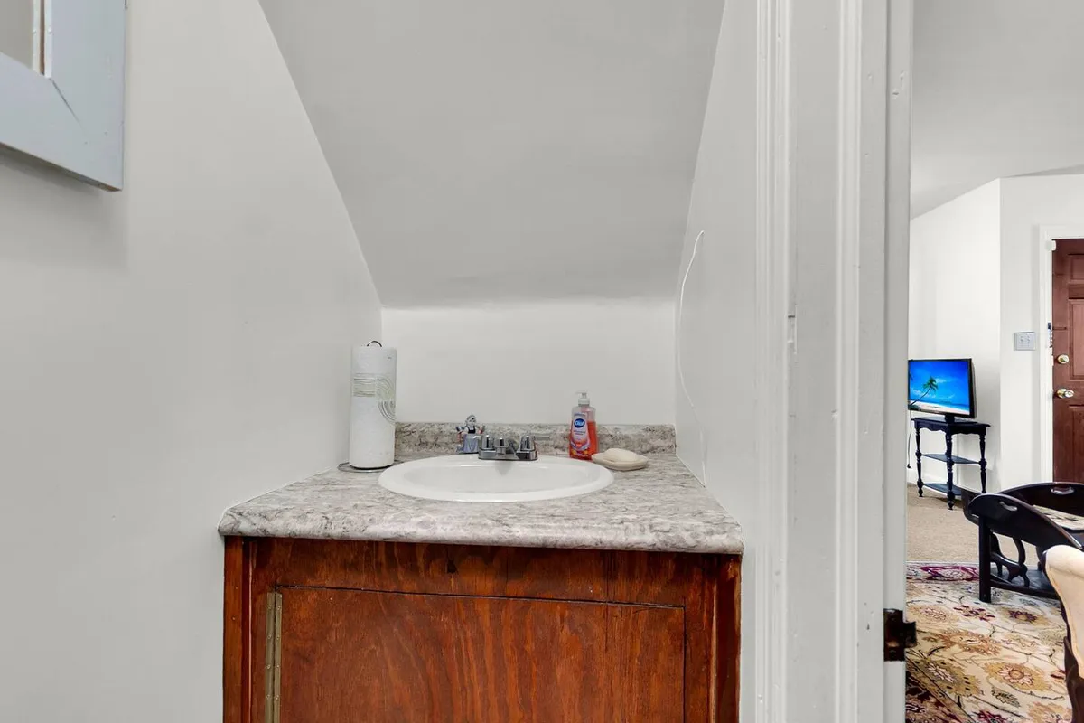 This image displays a practical and inviting bathroom vanity area with a sink, countertop, and mirror. The uncluttered design and thoughtful lighting evoke a sense of comfort and practicality, ideal for daily routines or a quiet moment of self-care.