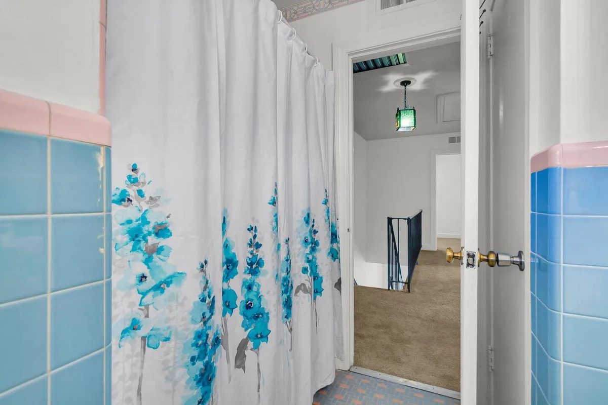 This interior image features a bathroom with a cheerful floral shower curtain, blue tiled walls, and a green pendant light. The setup immediately conveys a bright, clean, and inviting space for both quick morning showers and relaxing baths. The modern fixtures and playful color palette align with the section’s focus on comfort and convenience.