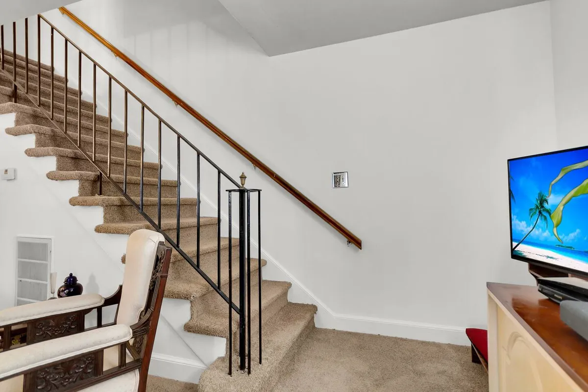 A relaxed corner of the living room with a staircase, a cozy chair, and a television. Natural light filters in, offering a space for quiet moments, movie watching, or connecting with others.