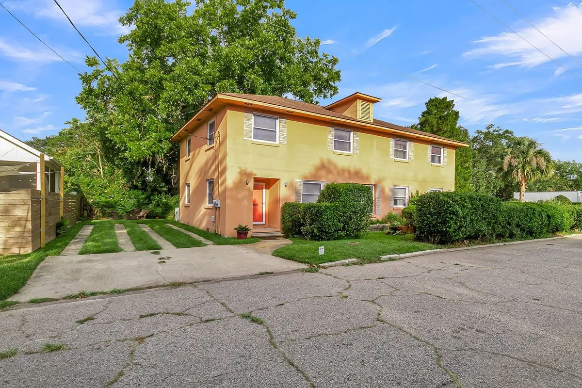 This exterior shot features the townhouse’s bright orange door, surrounded by lush greenery and a well-maintained lawn. The inviting porch area hints at a welcoming, social atmosphere suitable for gatherings.
