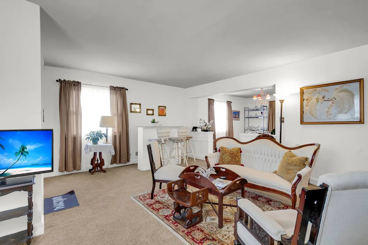 The image showcases a spacious and inviting living area with a comfortable sofa set, a large TV, a stylish bar area, and tasteful decorative artwork. The arrangement is perfect for relaxing, socializing, or entertaining, all set in a bright, welcoming atmosphere.